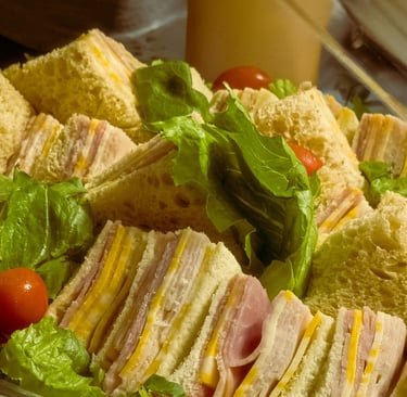 Freshly prepared ham and cheese finger sandwiches with lettuce and cherry tomatoes on a catering platter.