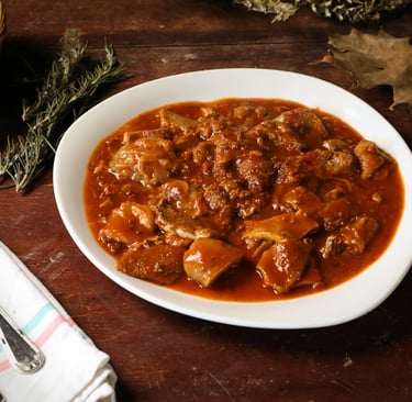 A white plate of traditional Italian tripe stew in tomato sauce on a rustic wooden table.