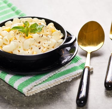 Creamy macaroni and cheese in a black bowl with a gold spoon and fork on a green napkin.