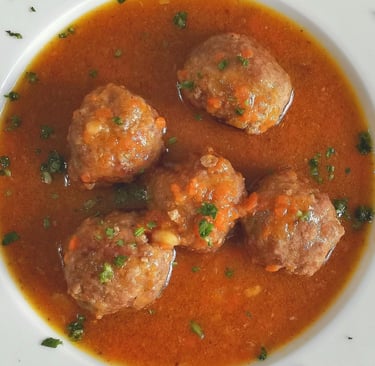 Beef meatballs in savory tomato vegetable broth served in a white bowl with herbs.