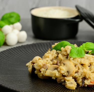 Creamy mushroom risotto with fresh basil leaves served on a textured black plate.