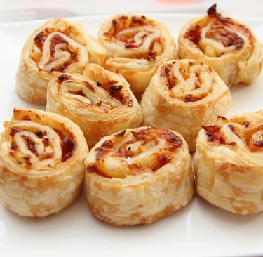 Golden brown savory puff pastry pinwheels with ham and melted cheese served on a white plate.