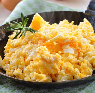 Fluffy scrambled eggs in a cast iron skillet with fresh rosemary and a side of toasted bread.
