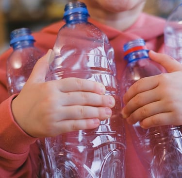 A person in a pink hoodie holding several empty clear plastic water bottles for recycling.