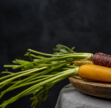 Freshly harvested heirloom rainbow carrots with green tops on a wooden plate against a dark background.