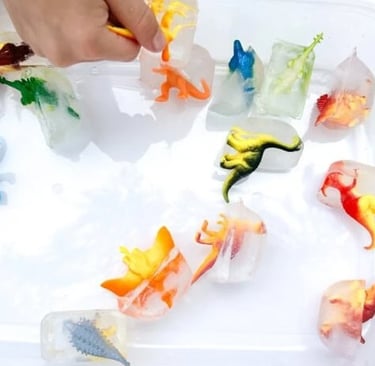 A child's hand picking up colorful toy dinosaurs frozen in ice cubes for a sensory science activity.