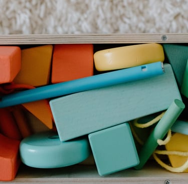 A collection of colorful wooden building blocks and geometric shapes stored in a wooden toy box.