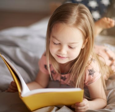 a little girl reading a book in bed