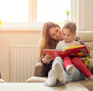 a woman sitting in a chair with a child and teaching reading