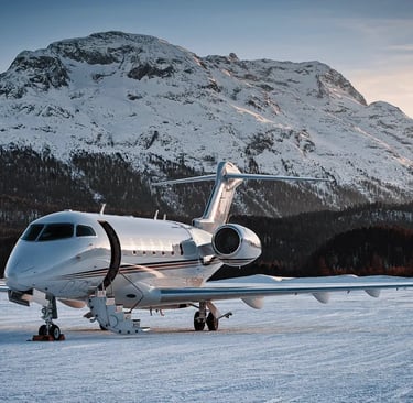 Bombardier Challenger 350 sitting on a snowy ramp with mountains behind