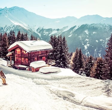 Verbier in winter, with a snow covered lodge, skier, pine trees and snow capped mountains.