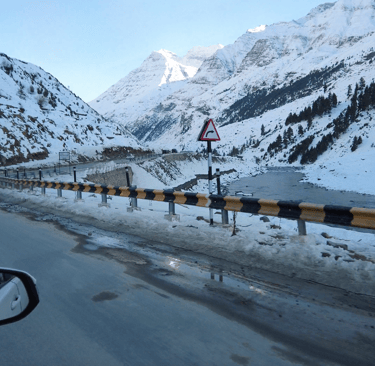 Car driving down a snow-covered mountain road from Manali to Sissu in Himachal Pradesh