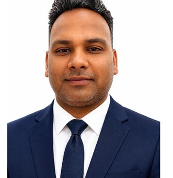 Professional headshot of a smiling Indian man in a dark blue suit and tie, looking directly at the camera.