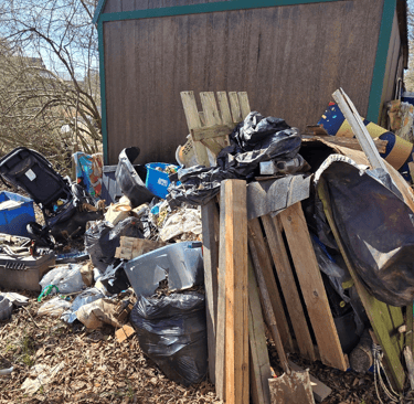 Storage building surrounded by trash, old stroller, old fencing, and more.