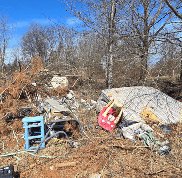 Image of a yard full of debris and trash, old mattresses, car toy, plastic shelf, yard debris.