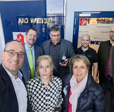 Gruppenfoto von sieben Personen in Businesskleidung bei einem Besuch in einem modernen Firmengebäude
