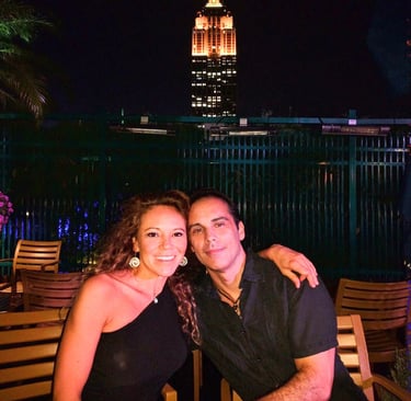 Travel bloggers on New York City rooftop at night with illuminated Empire State Building in backgrou