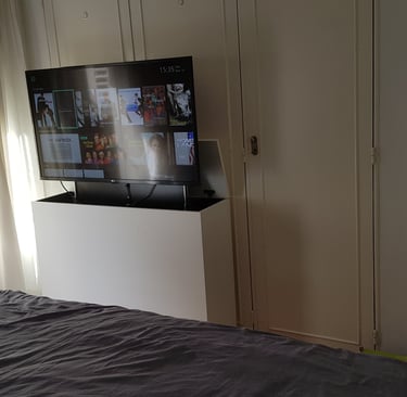 Dormitorio pequeño con mueble para ocultar TV y sistema de elevación motorizada frente a la cama