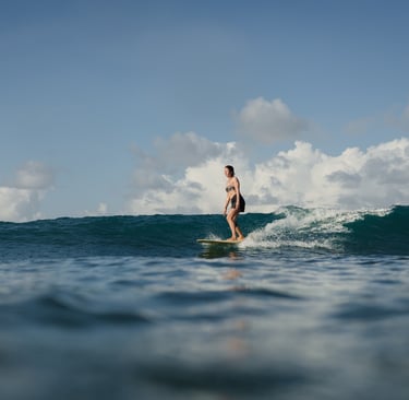 Woman taking surf lessons at a surf school in Kuta Lombok, riding a wave on a sunny ocean day