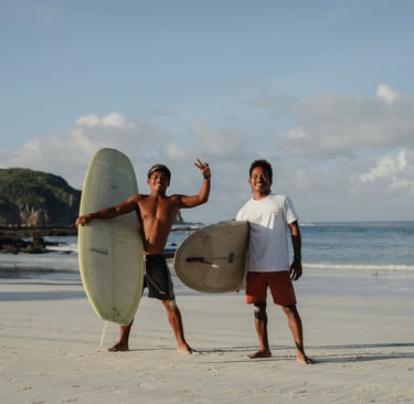 Two surf instructors at a surf school in Kuta Lombok holding boards on beach, offering surf lessons.