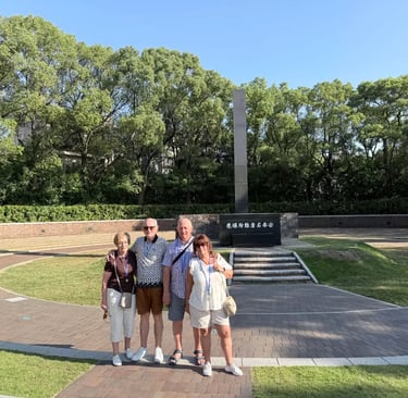 Four elderly travelers standing quietly in front of the atomic bomb hypocenter marker in Nagasaki