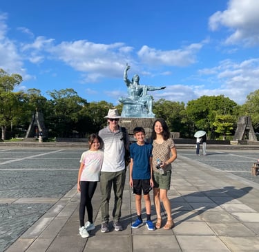 A family of four standing respectfully in front of the Peace Statue at Peace Park in Nagasaki