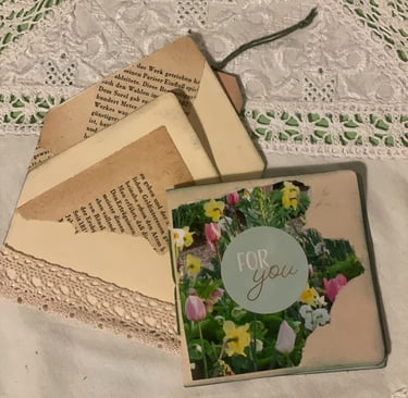 Handmade gift card with floral design and vintage book page fragments on a white lace doily.