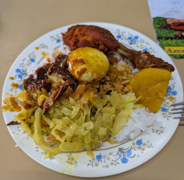A plate of Nasi Kandar with fried chicken, boiled egg, cabbage, and curry gravy.