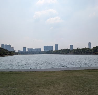 Wide view of Benjakitti Park lake with Bangkok city skyline skyscrapers in the background.