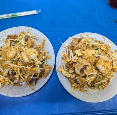 Two plates of authentic Char Kway Teow with prawns and bean sprouts on a blue table.