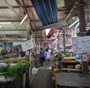 bustling Malaysian wet market with fresh vegetables, produce stalls, and shoppers under a canopy.