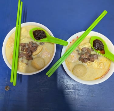 Two bowls of authentic Malaysian curry mee noodle soup with cockles, fish balls, and spicy sambal.
