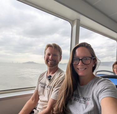 A smiling couple sits on a ferry boat to Penang with a scenic ocean view through the window.