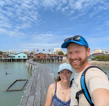 A smiling couple taking a selfie on a wooden pier over the water with stilt houses in the background