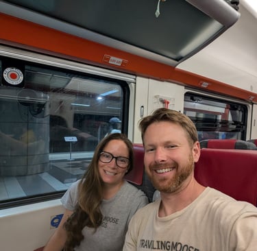 Don & Samantha weaing Traveling Moose and Bus shirts sitting on a train with red seats during a trip.