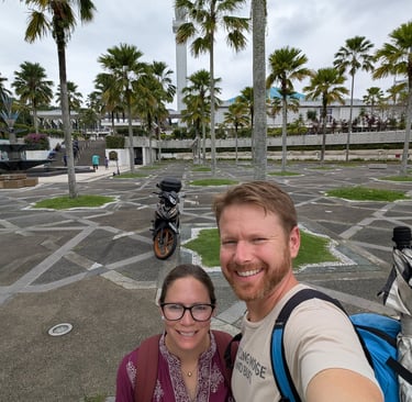  Don and Samantha take selfie at the National Mosque of Malaysia with palm trees and a minaret.
