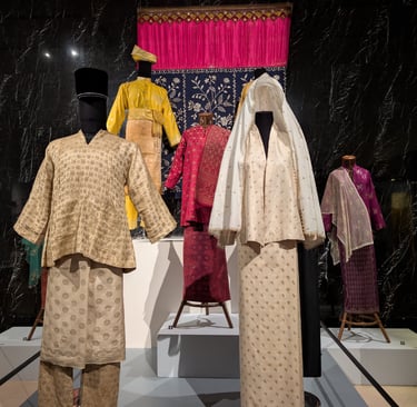 Traditional Malay Baju Kurung and Baju Melayu formal attire displayed on mannequins in a museum.