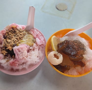 Two bowls of Malaysian lemon shaved ice and Ice Kacang desserts with peanuts and lychee.