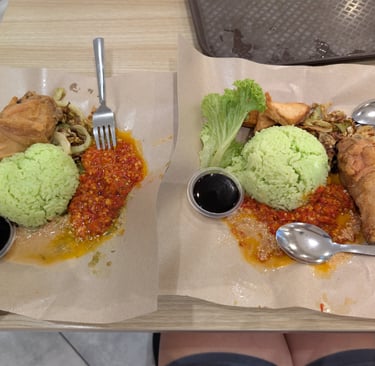 Two plates of Malaysian Nasi Lemak with green rice, fried chicken, and spicy sambal sauce.