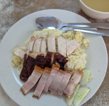 boiled chicken rice plate with roasted pork belly, char siu, and cucumber slices.