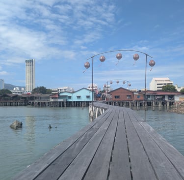 A wooden jetty at Jetty in Penang, Malaysia, with traditional stilt houses and the Komtar building in the distance.