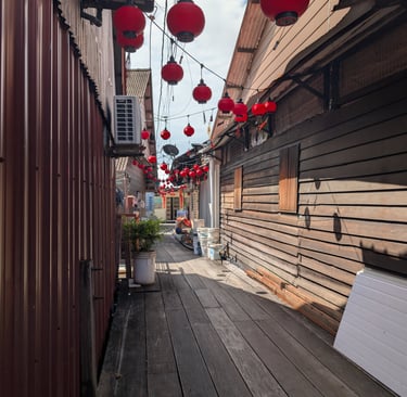 Red Chinese lanterns hanging over a narrow wooden boardwalk alley in a traditional village. Lim Jetty