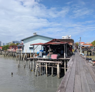 Traditional wooden stilt houses and jetties at the Lim Jetty of George Town, Penang, under a blue sky.