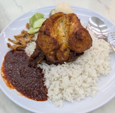 Malaysian Nasi Lemak plate with crispy fried chicken, coconut rice, spicy sambal, and anchovies.