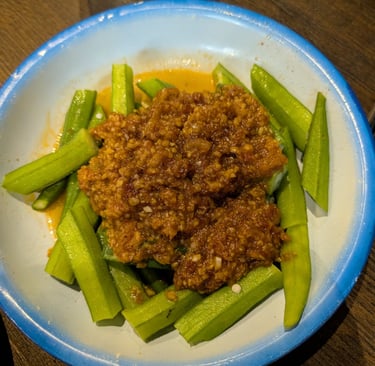 Steamed okra pieces topped with savory minced meat sauce in a blue-rimmed white bowl.