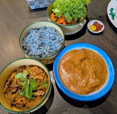 Peranakan Nyonya cuisine featuring blue pea rice, chicken curry, and stir-fried vegetables in tiffin carriers.