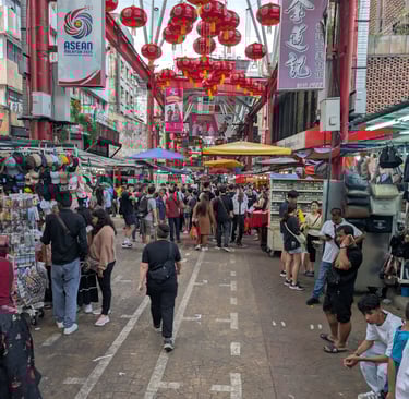Crowded Petaling Street market in Kuala Lumpur Chinatown with red lanterns and street vendors.