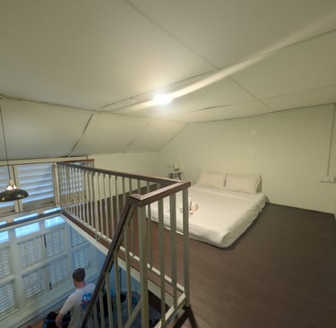 A loft bedroom with a white mattress on a dark wood floor and a metal railing overlooking the stairs