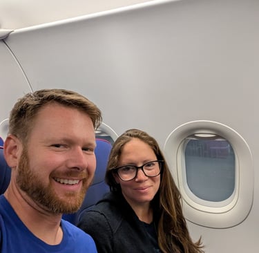 A smiling couple taking a selfie while sitting in their seats on a Wizz Air airplane flight.