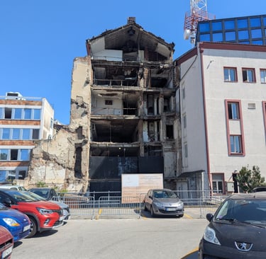 A multi-story bombed Radio Television ruins in Belgrade under a clear blue sky next to a parking lot